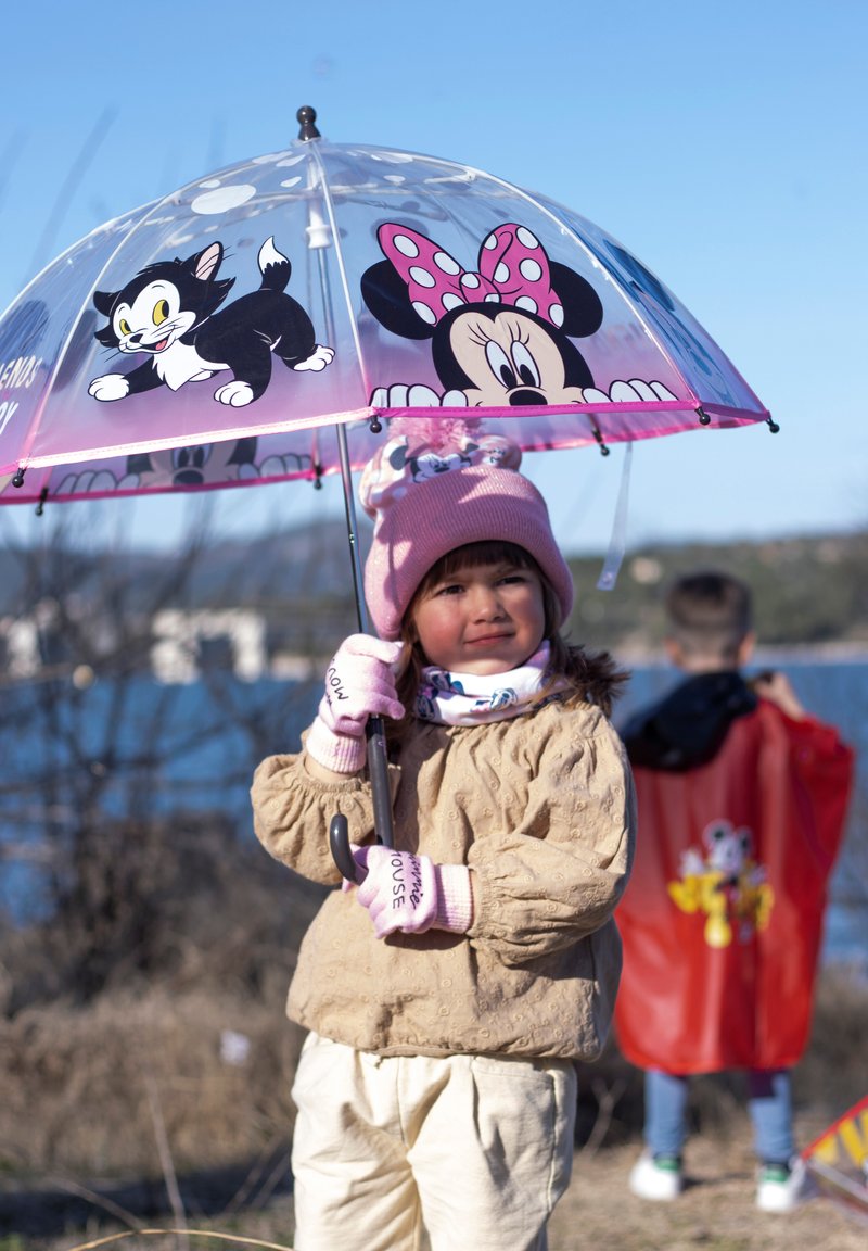 Transparante plastic paraplu met roze rand met cartoonfiguren Minnie Mouse en een zwarte kat. Kind met een beige pufferjack en handschoenen.