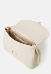 Sac à main en cuir crème avec fermoir doré, ouvert pour montrer la doublure en satin lisse et la poche intérieure.