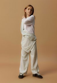Haut rose clair à manches longues avec des rayures blanches, associé à un pantalon de jogging gris surdimensionné. Présente une coupe décontractée et une taille à cordon, porté de manière décontractée.