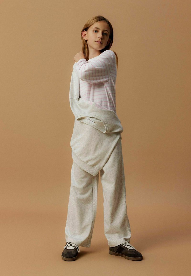 Haut rose clair à manches longues avec des rayures blanches, associé à un pantalon de jogging gris surdimensionné. Présente une coupe décontractée et une taille à cordon, porté de manière décontractée.