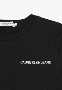 Czarna bawełniana koszulka z okrągłym dekoltem, z białym, haftowanym logo "CALVIN KLEIN JEANS" na froncie. Gładka tekstura, swobodny design.