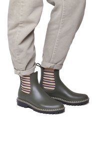 Bottes de cheville en caoutchouc vert avec des panneaux latéraux élastiques arborant un motif rayé marron et blanc. Semelle texturée noire avec des coutures blanches.
