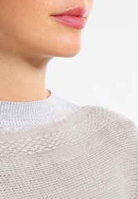 Maglione grigio lavorato a maglia con un motivo testurizzato e scollatura a coste, con una vista ravvicinata del colletto e dei piccoli dettagli.