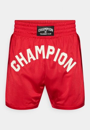 Κόκκινα αθλητικά σορτς με λείο υφή, με μαύρη ετικέτα και λευκά γράμματα "CHAMPION" που σχηματίζουν καμάρα στην πλάτη. Ελαστική μέση.