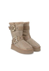 Beige enkelboots met studsdesign, gevoerd met nepbont, dubbele straps en decoratieve hardware details aan de zijkant. Vlakke platformzool.