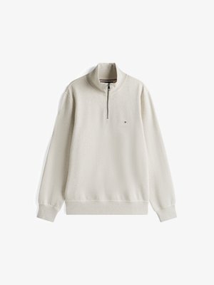 Vaalean beige vetoketjullinen huppari, jossa on korkea kaulus, ribbireunat hihansuissa ja helmassa, pehmeä rakenne, jossa on pieni logo vasemmassa rinnassa.