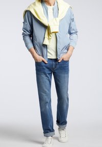 Jasnoniebieska nylonowa kurtka bomberka, żółty sweter zawiązany na szyi, jasny t-shirt, niebieskie dżinsy, białe trampki. Casualowy strój.