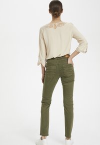 Beige blus med spetsdetaljer och nyckelhål baktill, i kombination med gröna skinny-byxor och vita sneakers, med fickor och figursydd design.