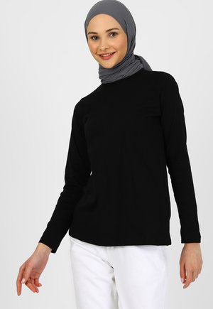 Maglietta nera a maniche lunghe realizzata in materiale morbido, con un design a girocollo. Il modello indossa un hijab grigio e pantaloni bianchi.