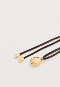 Φυλαχτό σε χρυσό χρώμα με σχήμα σταγόνας, σε σκούρο καφέ κορδόνι, με δύο μικρότερες σταγόνας ως διακοσμήσεις, λεία υφή και λαμπερό φινίρισμα.