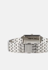 Montre en acier inoxydable avec un cadran rectangulaire, bracelet en maillons métalliques, finition polie et gravure "FOSSIL" sur le fermoir.
