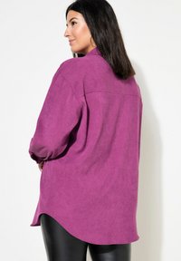 Camicia in velluto a coste viola con maniche lunghe, orlo curvo e vestibilità comoda, dotata di spalla posteriore e texture morbida.