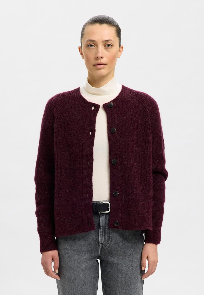 Bordo megzta kardigano su apvalia iškirpte, sagų užsegimu ir ilgomis rankovėmis, derantis su šviesiu golfu ir pilkais džinsais.