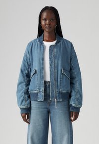 Jeans-Bomberjacke in Hellblau mit gerippten Bündchen an Ärmelenden und Saum, mit durchgehendem Reißverschluss, zwei seitlichen Taschen und abgenähten Details.