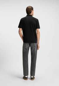 Czarna koszulka polo z płaskim kołnierzykiem, połączona z szarymi spodniami o prostym kroju i czarnymi sneakersami. Gładka tkanina, prosty fason, brak widocznych wzorów.