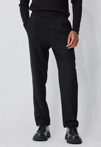 Pantalon noir avec une ceinture élastique confortable, doté de deux poches avant et d'une coupe droite. Porté avec des chaussures noires.