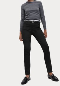 Svarta smala jeans i kombination med en grå långärmad skjorta. Outfitsen kompletteras av svarta loafers. Slät tyg, åtsittande design.