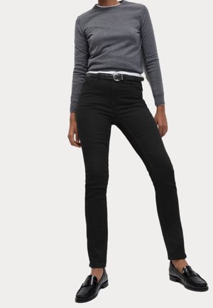 Jean skinny noir associé à une chemise à manches longues grise. La tenue est complétée par des mocassins noirs. Tissu lisse, design ajusté.