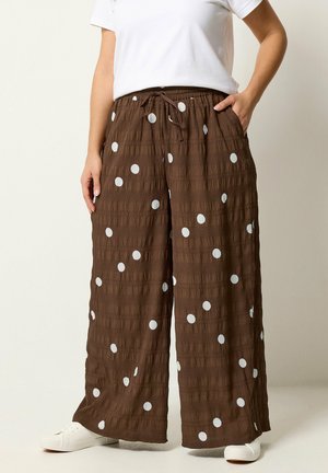 Brązowe szerokie spodnie w białe kropki, elastyczny pas ze sznurkiem, noszone z białymi trampkami i białą bluzką z krótkim rękawem.