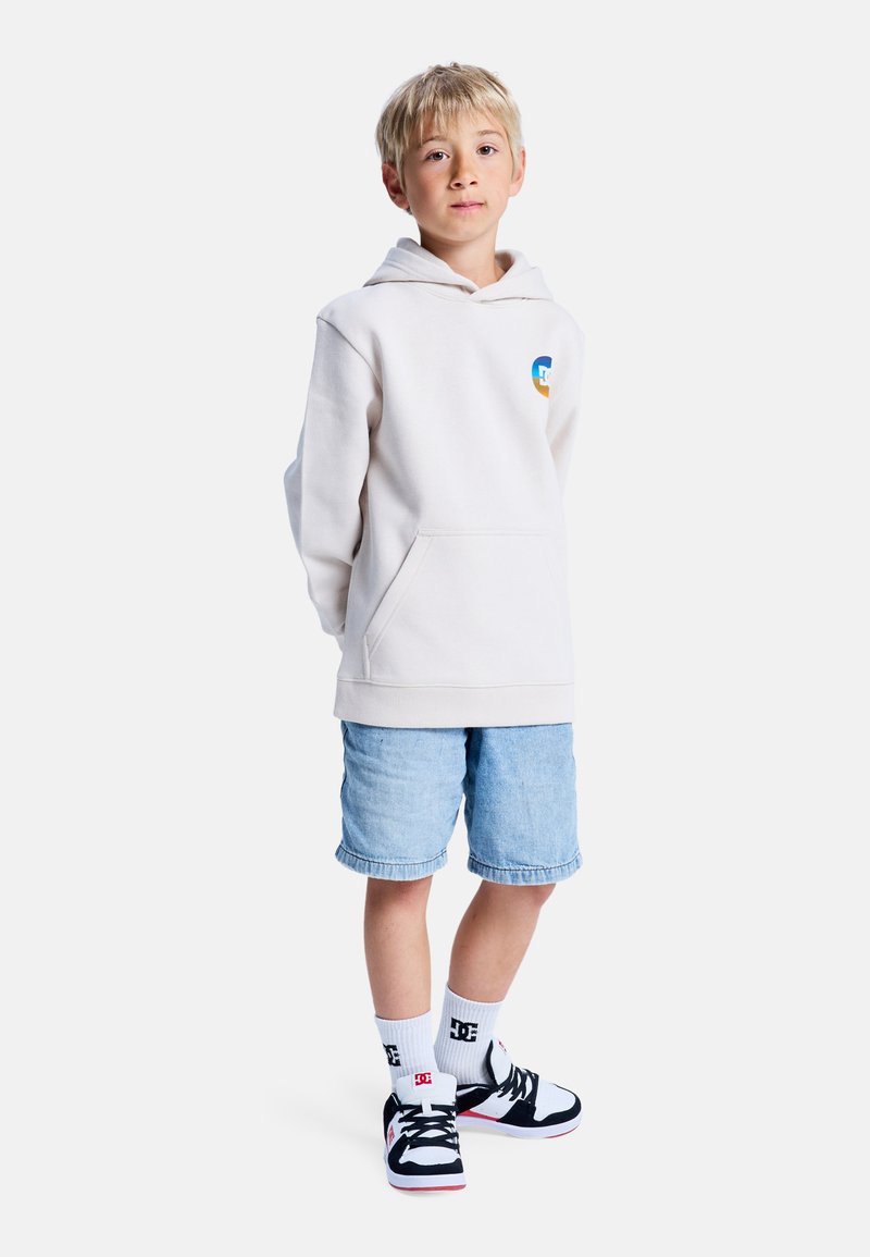 Sweat à capuche crème avec poche avant et petit logo, associé à un short en denim bleu clair, des chaussettes blanches et des baskets noir et blanc.