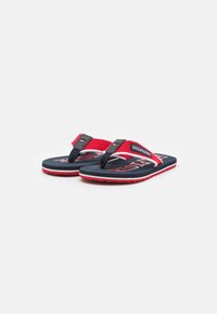 Røde og marineblå flip-flops med en tekstureret rem, prydet med et logo på forsiden, polstrede sorte såler og hvide detaljer langs kanterne.