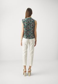 Top sin mangas de color verde con estampado floral, combinado con pantalones blancos ajustados y sandalias beige de tacón ancho. Tejido suave y ligero.