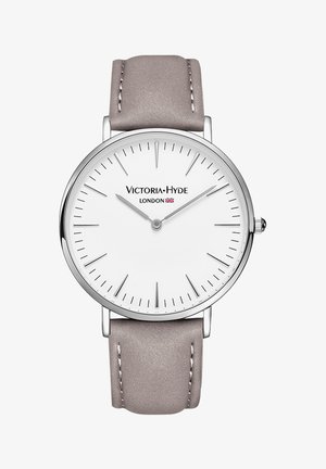 Reloj de acero inoxidable plateado con esfera blanca, correa de cuero gris, marcadores de hora delgados y un diseño minimalista. Nombre de la marca exhibido de manera prominente.
