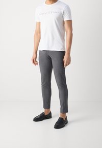 Bílý tričko s krátkým rukávem s potiskem "Marc O'Polo" v světlé šedé; v kombinaci s obtaženými šedými kalhotami a černými slip-on mokasíny.