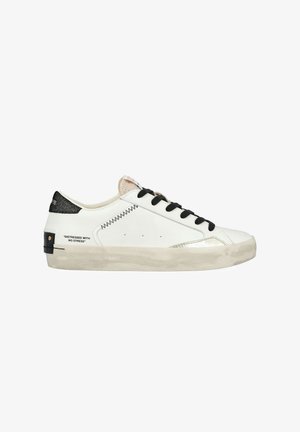 Sneaker in pelle bianca con lacci neri, dettagli metallici argentati e una robusta cappe nera testurizzata. Presenta cuciture decorative e testo stampato.