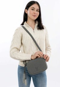 Šedá crossbody taška s texturovaným povrchem, obdélníkovým tvarem a odnímatelným třásním. Má dlouhý, nastavitelného popruhu a detail loga.