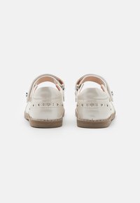 Parte trasera de sandalias de cuero blanco con un tacón redondo, correa ajustable y patrones decorativos en forma de corazón calados. Textura suave y suela de color neutro.