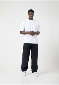 Witte katoenen T-shirt met korte mouwen, gecombineerd met donkergrijze denim broek. Witte sneakers met groene accenten. Casual fit, minimalistisch ontwerp.