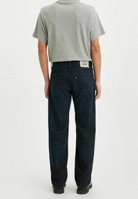 Jeans blu scuro con una classica vestibilità dritta, dotati di tasche posteriori e un'etichetta bianca in vita. Abbinati a una maglietta grigia.