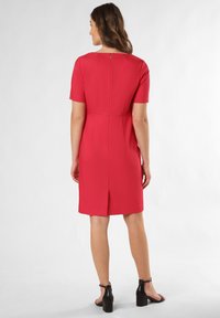 Czerwona sukienka z krótkim rękawem o prostym kroju, z zamkiem błyskawicznym z tyłu i rozcięciem na dole. Gładka tekstura tkaniny i dopasowany krój.