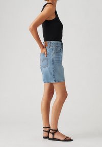 Falda de mezclilla azul claro con corte recto, cinco bolsillos y un ligero desgaste en el dobladillo. Se lleva con una camiseta sin mangas negra y sandalias negras.