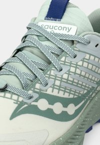 Heled roheline spordijalats, millel on võrgu pealmine osa koos tekstuuriga mustriga, hallad paelad ja sinine kontsapael Saucony logo kaubamärgiga.