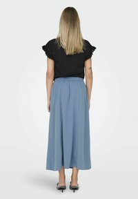 Haut noir avec des manches à volants, associé à une jupe plissée bleu clair de longueur chevilles, complété par des sandales à talons hauts noires.
