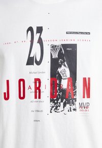 Vit bomullströja med en grafisk bild av Michael Jordan i aktion. Röda och svarta texter lyfter fram prestationer, med stora siffror och foton.