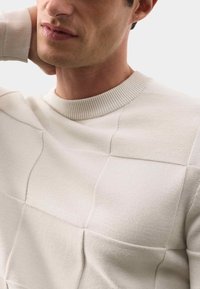 Helles beige Sweater mit einem strukturierten Rautenmuster und ribbeltem Kragen. Besteht aus einem weichen Strickmaterial und hat eine lockere Passform.