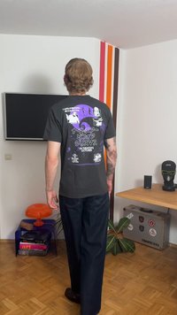 Svart bomulls-T-shirt med ett lila grafiskt tryck på baksidan, inklusive text och tecknade figurer. Avslappnad passform och korta ärmar.