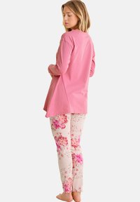 Un haut à manches longues rose et un pantalon à motifs floraux de couleurs claires, avec de grandes fleurs roses et des accents délicats. Tissu doux.