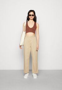 Top cropped castanho, calças largas de cintura alta bege, ténis brancos com detalhes em vermelho e uma mala tote bege, usados com óculos de sol escuros.
