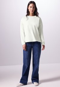 Lichtgroene, losse sweatshirt met een geribde halslijn, gecombineerd met hoge, wijde donkerblauwe jeans en witte sneakers.