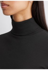 Schwarzes, geripptes Rollkragenoberteil mit körperbetontem Design und hohem Kragen, das eine glatte Textur und einen minimalistischen Stil betont.
