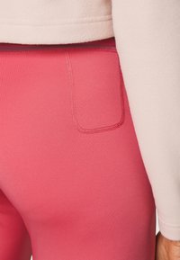 Rosa leggings med en slät yta, försedd med en sydd ficka. Matchas med en ljusfärgad, texturerad fleece-tröja.