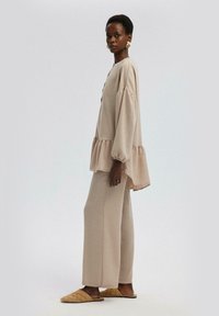 Top oversize de color beige claro con mangas abullonadas y dobladillo acampanado, combinado con pantalones sueltos de color beige a juego y sandalias tipo slip-on acolchadas.