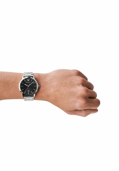 Linkes Handgelenk mit einer silbernen Metalluhr mit schwarzem Zifferblatt, minimalistischem Design und Datumsanzeige an einer Hand mit hellem Hautton.
