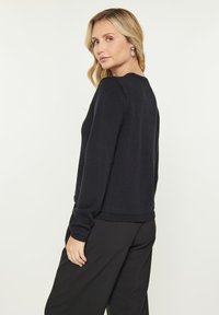 Pulover lung negru cu mânecă lungă dintr-un material moale, cu decolteu rotund și manșete curbate, având o croială lejeră și un design simplu.