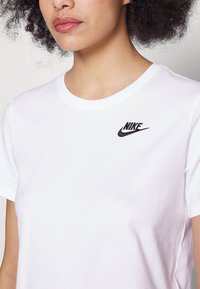 T-shirt en coton blanc avec un col rond et des manches courtes, présentant un petit logo Nike noir brodé sur la zone gauche de la poitrine.