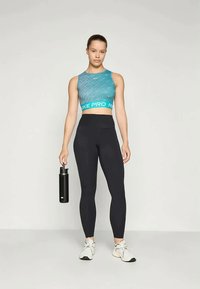 Nike Pro Sport-BH in Türkis mit strukturiertem Muster, kombiniert mit hochgeschnittenen schwarzen Leggings und hält eine schwarze Wasserflasche.